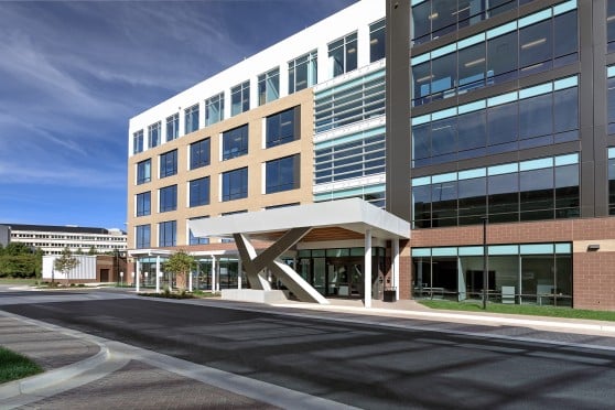 A digital rendering of a modern office building that use many different finishes. The columns are in the shape of the letter K