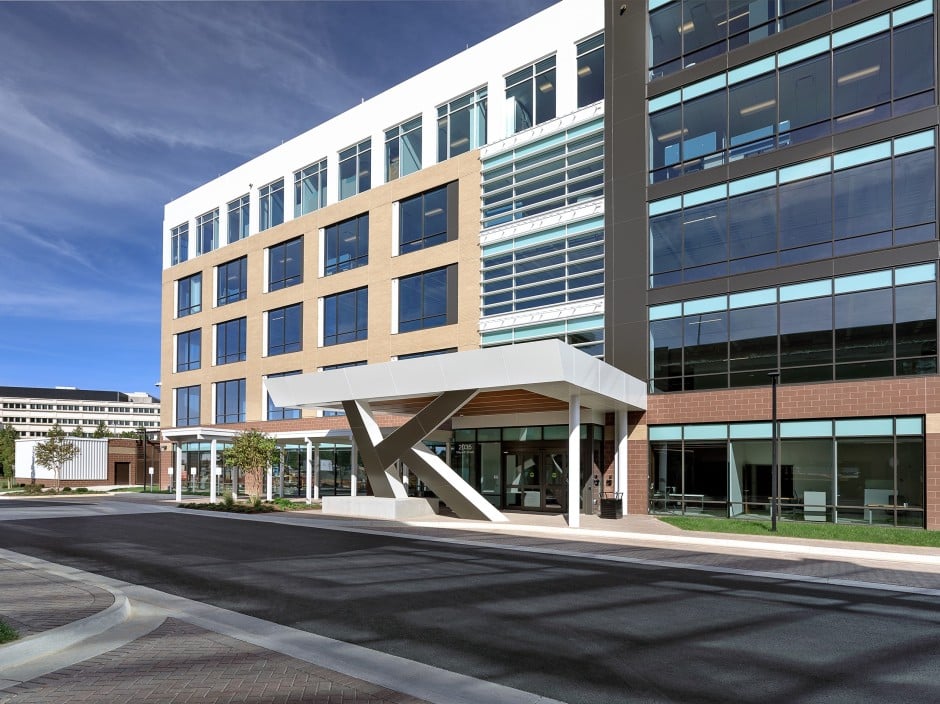 A digital rendering of a modern office building that use many different finishes. The columns are in the shape of the letter K