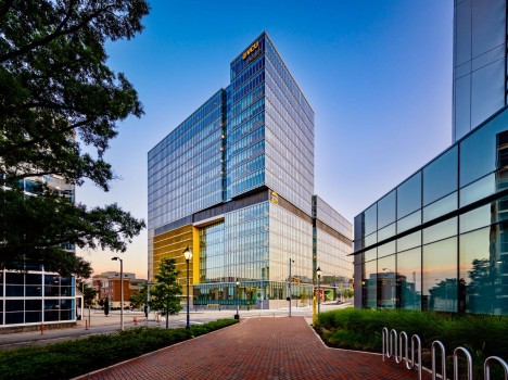 A modern high-rise office building at twilight with illuminated windows and the company logo ‘VCU Health’ at the top.