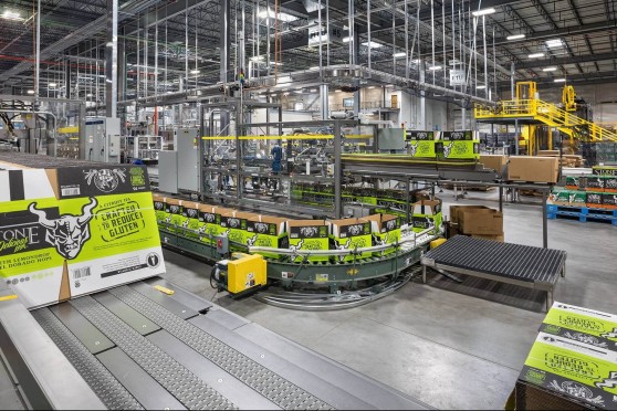 Many conveyer belts assemble and move green boxes inside a gray warehouse.