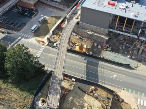 A bridge is constructed over a road, connecting a construction site to a large hill.