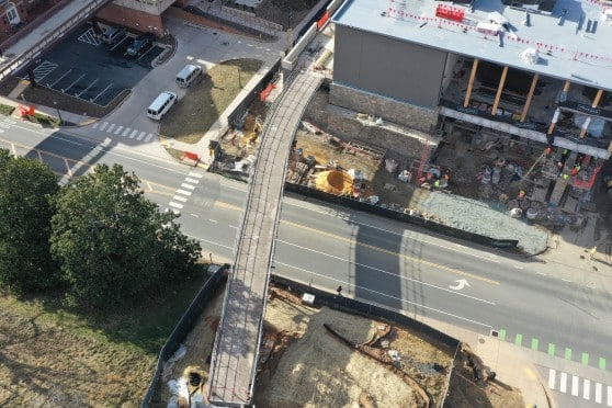 A bridge is constructed over a road, connecting a construction site to a large hill.