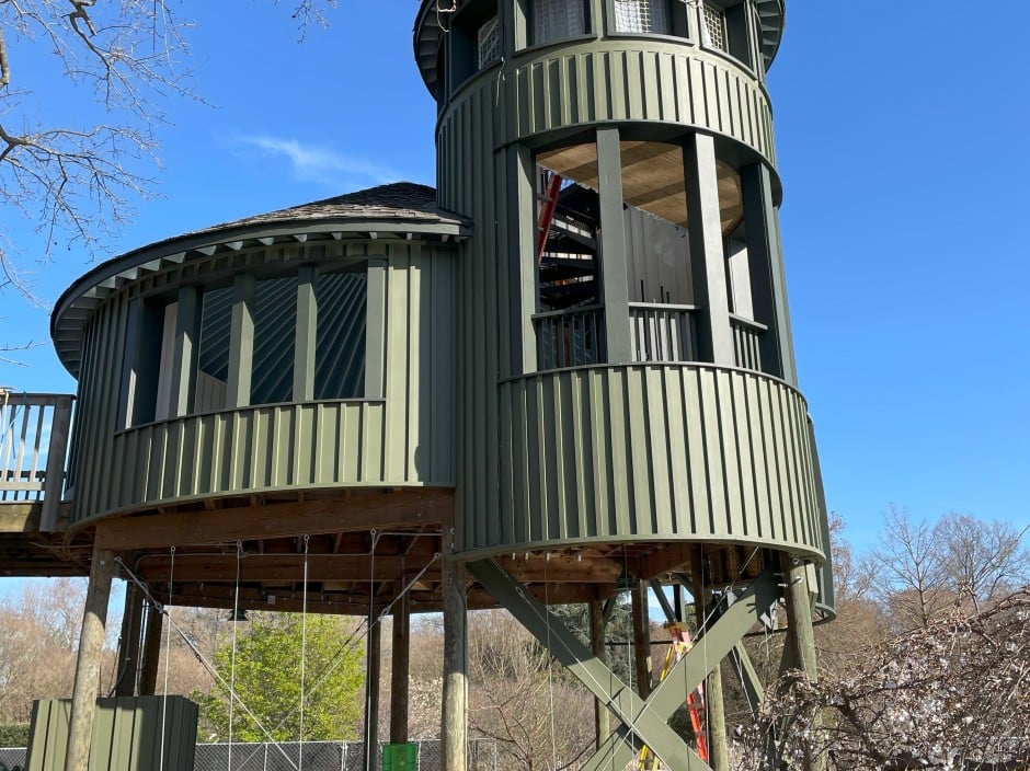 A green circular treehouse with a cone shaper roof is in front of a blue sky