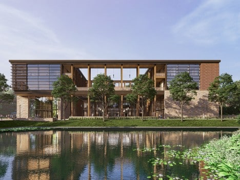 Image depicts a modern black metal building with wooden beams and windows. There is a body of water and plants in the foreground.
