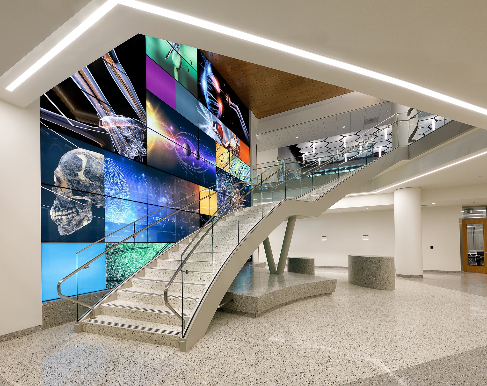 A glass staircase next to a large screen with many science related images on it.