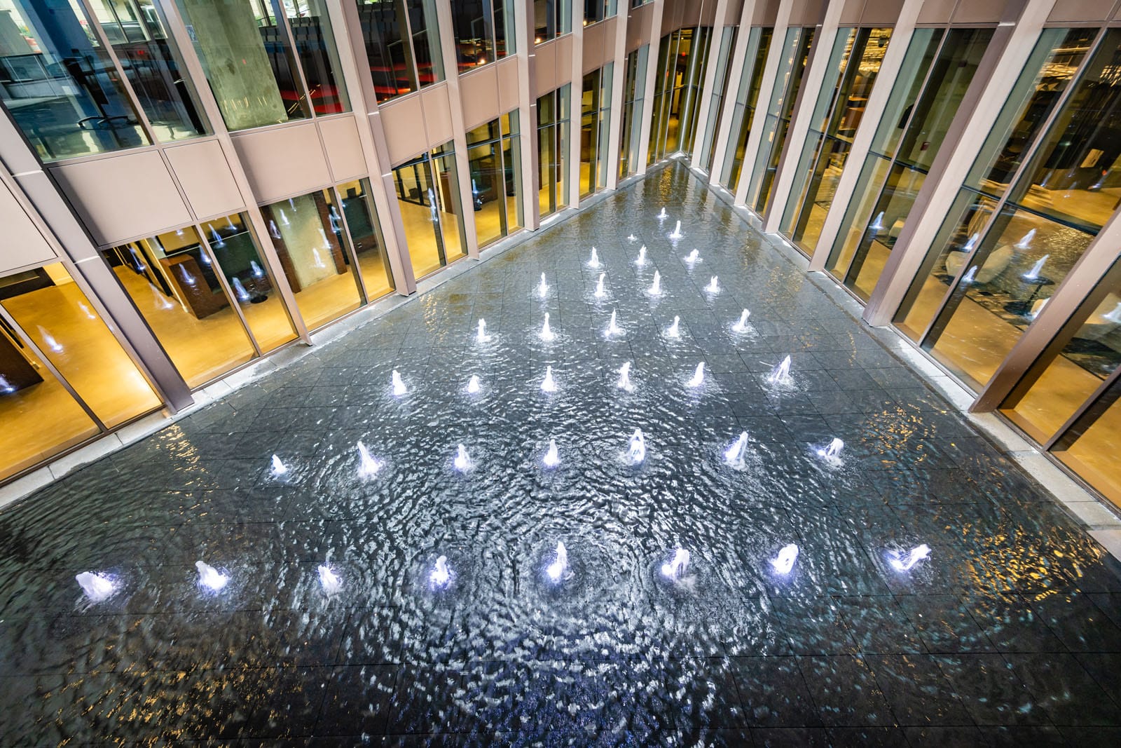 The view of a triangular water feature form the second floor Many small fountains sit inside a large pool, surrounded by windows.