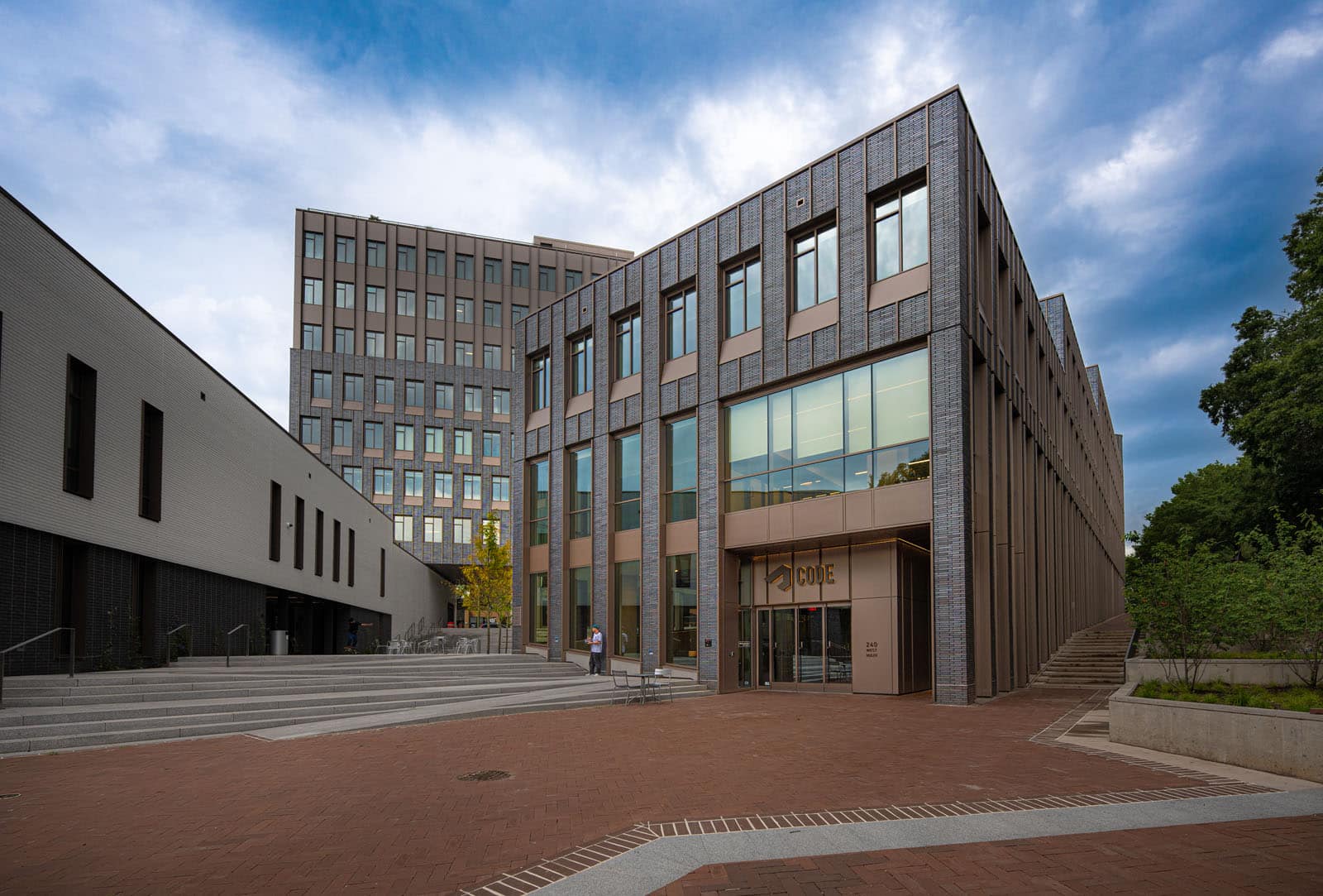 A modern building with a brick and glass facade and the word “CODE” above the entrance, surrounded by a cloudy sky.
