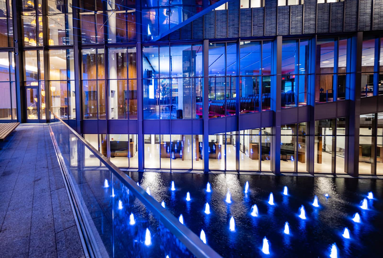 The view of a triangular water feature form the second floor Many small fountains sit inside a large pool, surrounded by windows. The small fountains are lit up blue.
