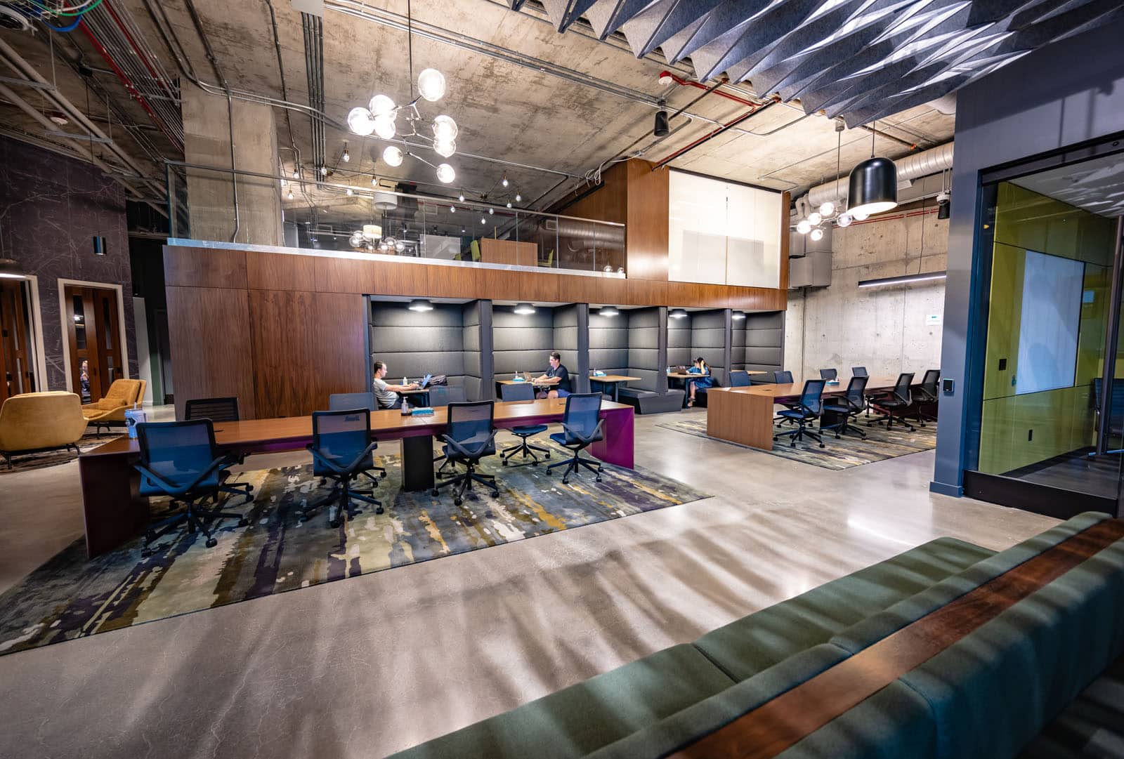 Conference tables and built in seating are seen in a modern workspace with wood, concrete, and steel walls.