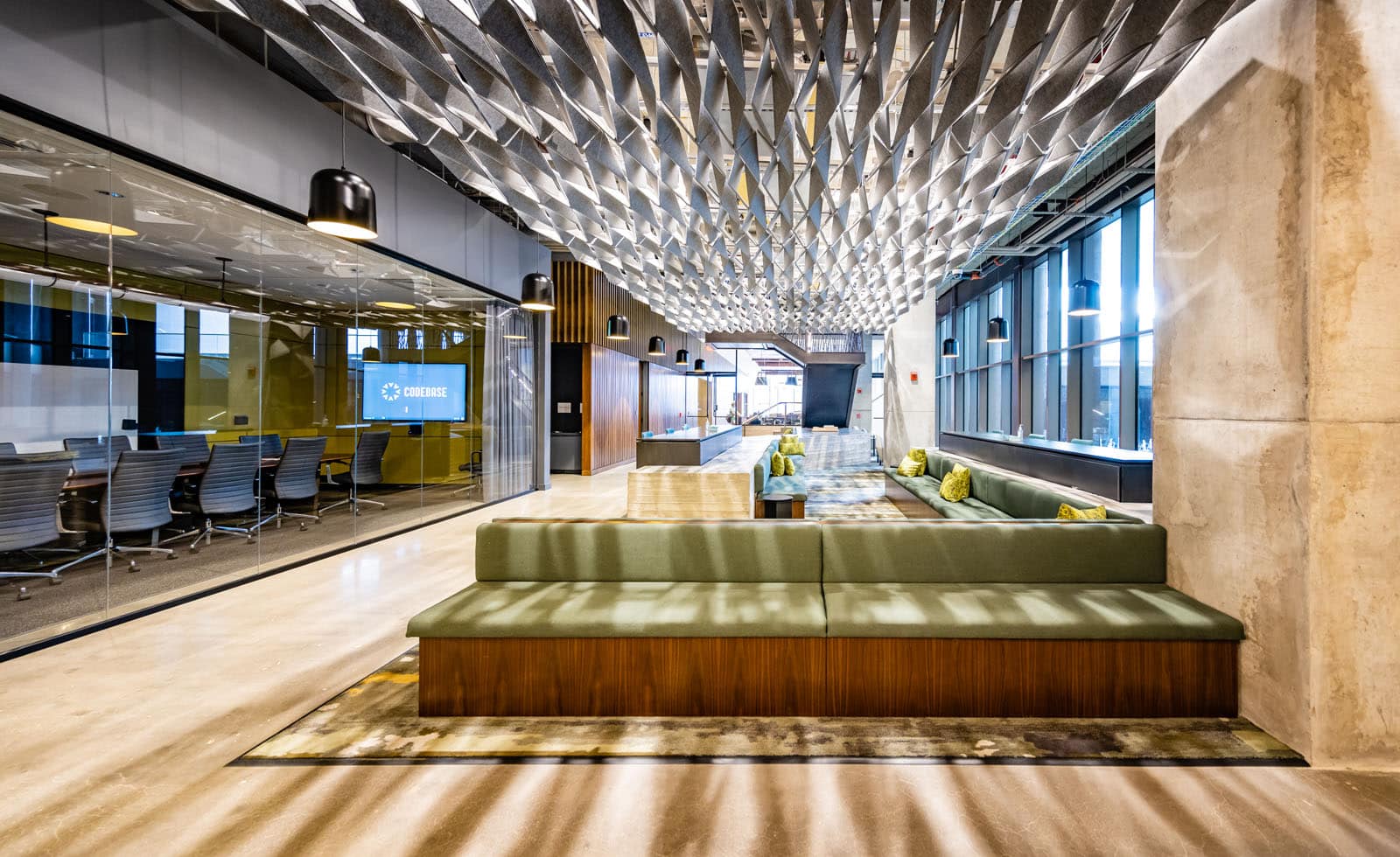 The image depicts a modern and spacious interior with a blend of eclectic furniture. The ceiling features an intricate geometric pattern, and large windows allow ample natural light. A conference room is seen through glass panels on the left.