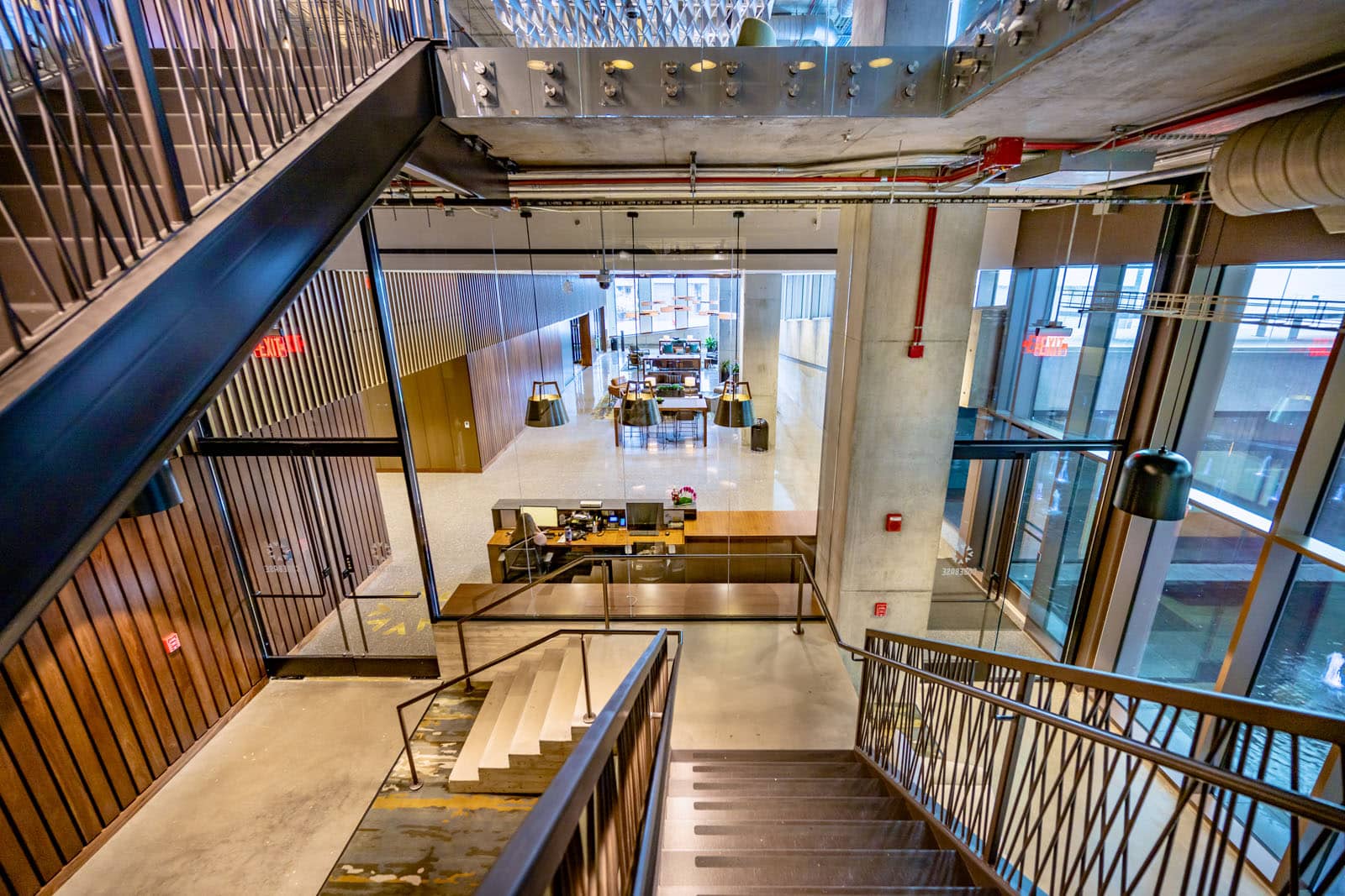 The view of a first floor lobby from the top of stairs. Room has concrete floors and walls with wooded furniture and panels.