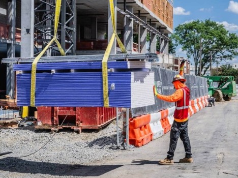 A man in construction safety equipment stands next to a pile of material being moved by a crane.