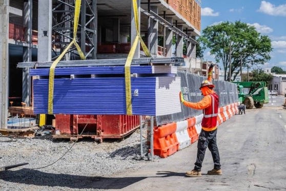 A man in construction safety equipment stands next to a pile of material being moved by a crane.