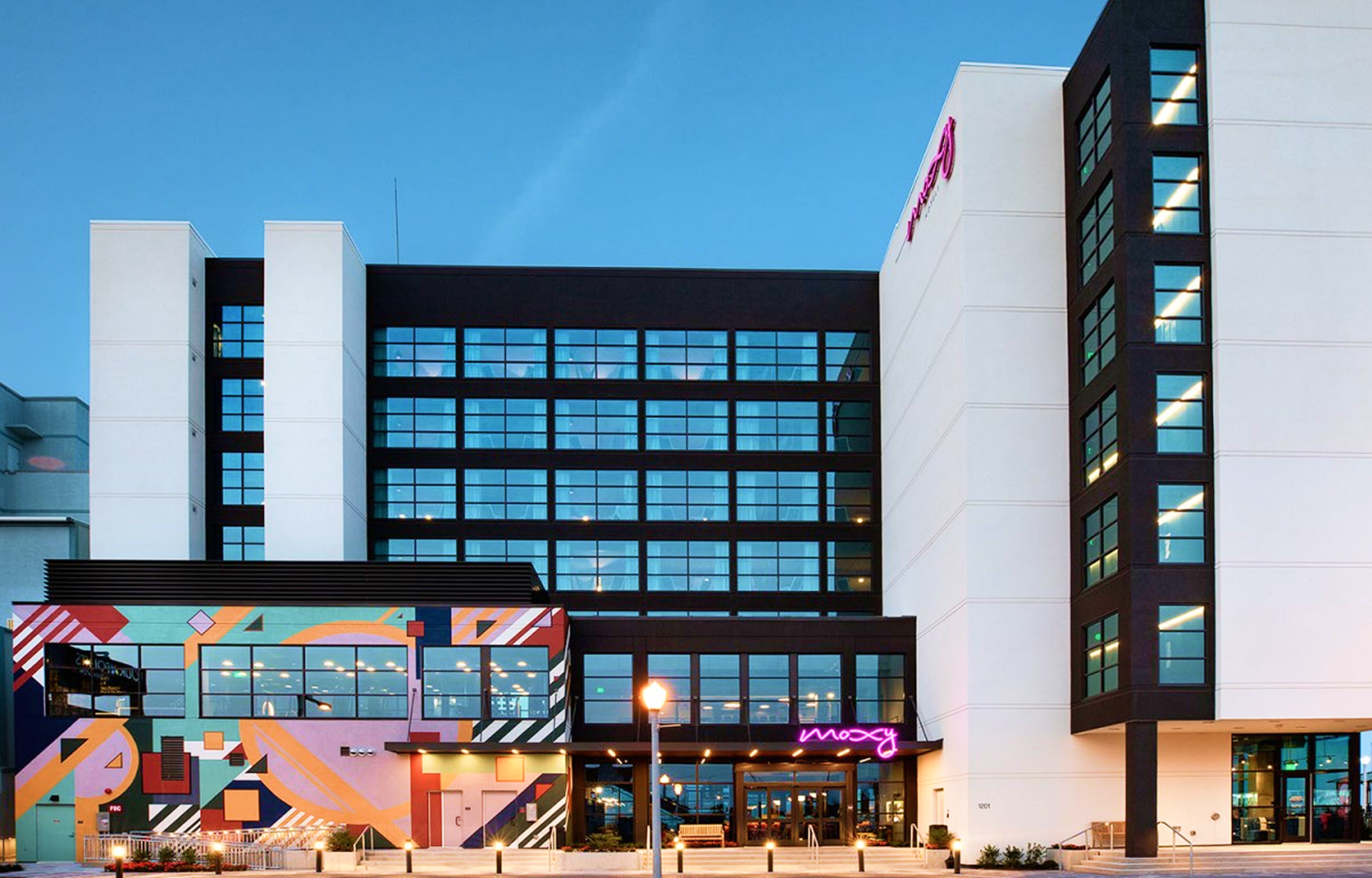 A large black and white hotel with a mural and a pink sign that says the Moxy.